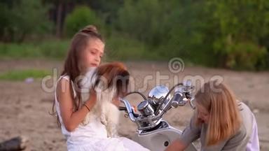 两个姐妹在一起玩得很开心。 两个女孩和一只狗在海边的摩托附近玩耍。 两个女孩在一起玩耍和交谈