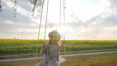 儿童在森林公园中摇摆自然，慢动作，可爱的小女孩肖像坐在自然的秋千上，日落的灯光