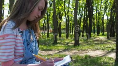女孩在公园画画。 一个关于大自然的少女。 穿牛仔工作服的漂亮女孩画画。