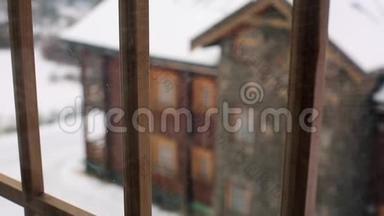 在大雪期间，透过窗户观看山村的木屋。 落在木屋上的雪
