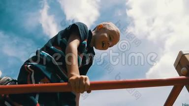 小男孩用手把酒吧吊起来，慢慢地在户外运动场和天空做运动