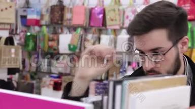 年轻的黑发男子戴着眼镜在书店的<strong>书架</strong>上<strong>看书</strong>。