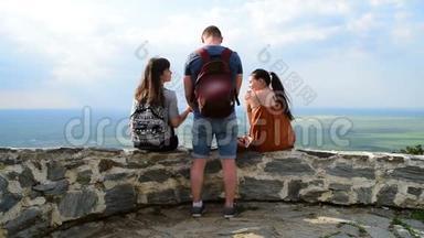 三个朋友一男两女<strong>分别</strong>在堡垒的墙上，高视角和山谷上休息