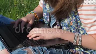 用手在笔记本电脑上打字。公园里的女孩正在笔记本电脑上打字。破旧的牛仔裤和手镯。