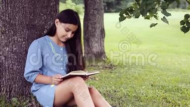 一个留着长发的漂亮小女孩读着一本书，坐在树下，梦见了一些令人愉快的事情