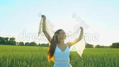 美丽的女孩，戴着围巾，随风飞翔，日落时在麦田里奔跑。 自由健康幸福观念