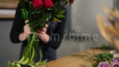 年轻迷人的女花店在花店里布置一束美丽的红玫瑰。 慢镜头