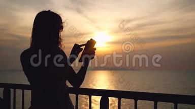 年轻的黑发女人戴着太阳镜站在游轮甲板上，用她的智能手机剪影。 <strong>飘摇</strong>的风