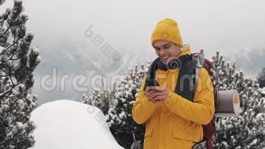 年轻的旅行者在徒步冬季旅行中使用智能手机。 白雪模糊的山角和湖。 旅行和
