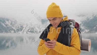年轻的旅行者在徒步冬季旅行中使用智能手机。 白雪模糊的山角和湖。 旅行和
