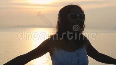年轻快<strong>乐</strong>的女士戴着太阳镜，在美丽的日落和美丽的海景中，用耳机听音<strong>乐</strong>，玩得很<strong>开心</strong>