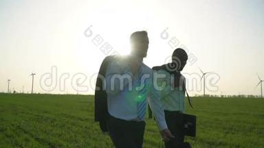 身穿商务服的黑人和白人正在绿色草地上行走，背景是可见的风力发电机