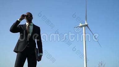 身穿商务服的黑人男士在风力发电机背景附近摘下太阳镜