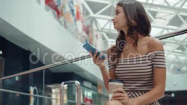 购物妇女微笑着拿着袋子在<strong>商场</strong>的电话里交谈。 带智能手机的漂亮女孩带着购物<strong>中</strong>心的行李