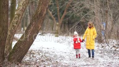 年轻的母女在冬季公园散步。 他们穿着鲜艳的羽绒服