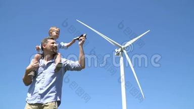 父亲把儿子扛在肩上，和他玩，对着风力发电机的背景射击