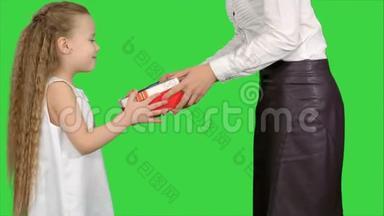 年轻迷人的母亲和她可爱的女儿在绿色屏幕上打开圣诞礼物，彩色钥匙