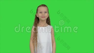 快乐美丽的小女孩在绿色屏幕上对着相机摆姿势，色度键