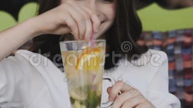 美丽的女孩用小管搅拌柠檬水，对着镜头微笑