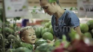 年轻的母亲和小女儿在超市挑选水果