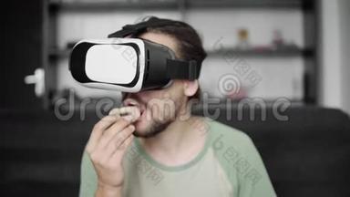 年轻留胡子的嬉皮士使用他的VR耳机显示器观看360视频，而坐在沙发上和吃