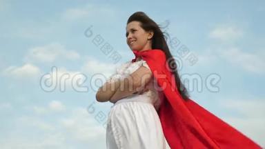 超级英雄女孩穿着红色斗篷站在田野上，斗篷在风中飘扬。 特写镜头。 女孩梦想<strong>成为</strong>一个