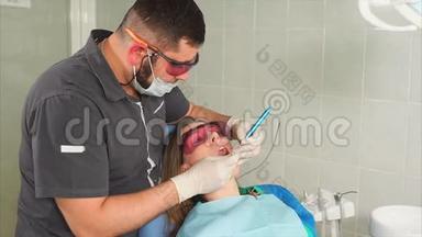 戴眼镜的<strong>牙齿矫正</strong>医生用激光给一个年轻女人美白<strong>牙齿</strong>
