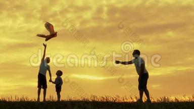 快乐的一家人爸爸和孩子们在草地上奔跑，夏天日落时放风筝