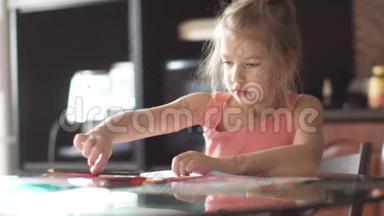 六岁的孩子坐在一张桌子旁画房子。 清晨阳光下的小女孩