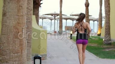 那个运动<strong>女孩</strong>在<strong>度假</strong>村拿着雨伞向沙滩跑<strong>去</strong>。 早晨慢跑一个苗条的黑发女人。