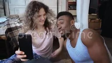 美丽的多民族夫妇在智能手机上拍摄自拍照片。 女人拿着智能手机，男人吻她笑。