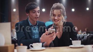 年轻漂亮的一对夫妇兴高采烈地讨论着他们在智能手机上看到€™什么，在约会中喝咖啡。