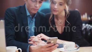 一对年轻夫妇在手机屏幕上滚动浏览照片€™讨论他们在现代城市咖啡馆的一个©中热闹地约会。