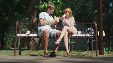 快乐的一对夫妇吃热狗，在城市公园的长凳上玩得很开心。 4K，慢动作。