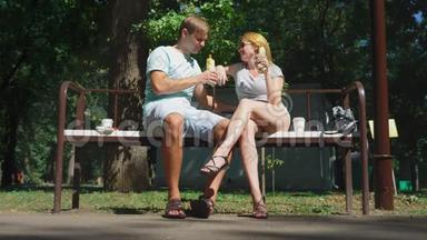 快乐的一对夫妇吃热狗，在城市公园的长凳上玩得很开心。 4K，慢动作。