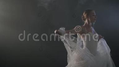 优雅的芭蕾舞演员穿着白色连衣裙，在黑暗中用灯光和烟雾舞蹈古典或现代芭蕾的元素