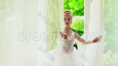 美丽的小芭蕾舞女看着窗外的大自然。 穿着白色短裙的小女孩在窗边