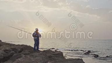 老渔夫站在海边的岩石上，在夕阳下钓鱼