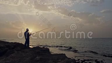 老渔夫站在海边的岩石上，在夕阳下钓鱼