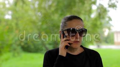 戴太阳镜的女孩结束了电话交谈，在绿色公园挂断了电话