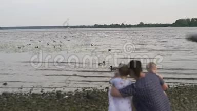 年轻的母亲带着她的小女儿在河边喂天鹅和<strong>小鸭</strong>子，小鸟在河边吃面包，穿着点缀的裙子