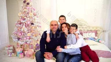 幸福快乐的家庭肖像，两个哥哥`孩子和慈爱的父母<strong>坐在</strong>卧室的<strong>床上</strong>，<strong>上</strong>面挂着节日树