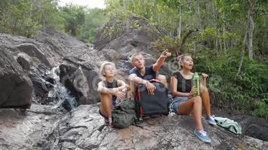 一群年轻游客在瀑布旁休息，欣赏大自然的美丽。 高清慢速运动。 泰国。