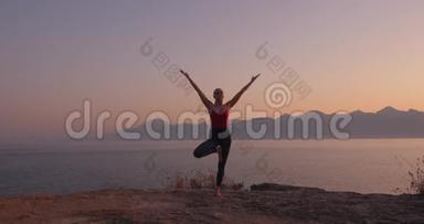穿红色衣服的白人妇女在日落时在海边的悬崖上练习瑜伽，放松<strong>身心</strong>。