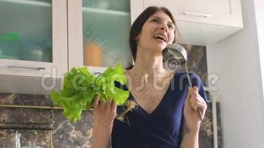 有趣的女人在厨房做饭的时候，用大勺子<strong>和</strong>莴苣<strong>跳舞唱歌</strong>