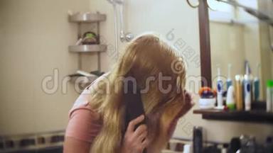 女人<strong>掉头</strong>发，一个金发的女人在镜子前的浴室里梳着长发。 头发留在上面