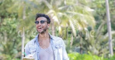 西班牙男人在棕榈树上喝椰子鸡尾酒，开心地微笑年轻的拉丁裔游客
