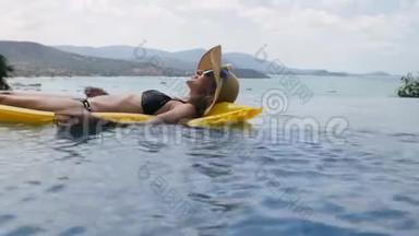 快乐的女人在游泳池里的黄色充气床垫上放松。