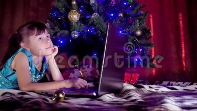 圣诞树下有笔记本电脑的女孩。 在<strong>新年</strong>里，孩子在一棵树下，<strong>手提</strong>电脑。 树下的一个小女孩
