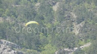 橙色条纹的黄色滑翔伞在灰色大岩石的背景下在美丽的山区飞行